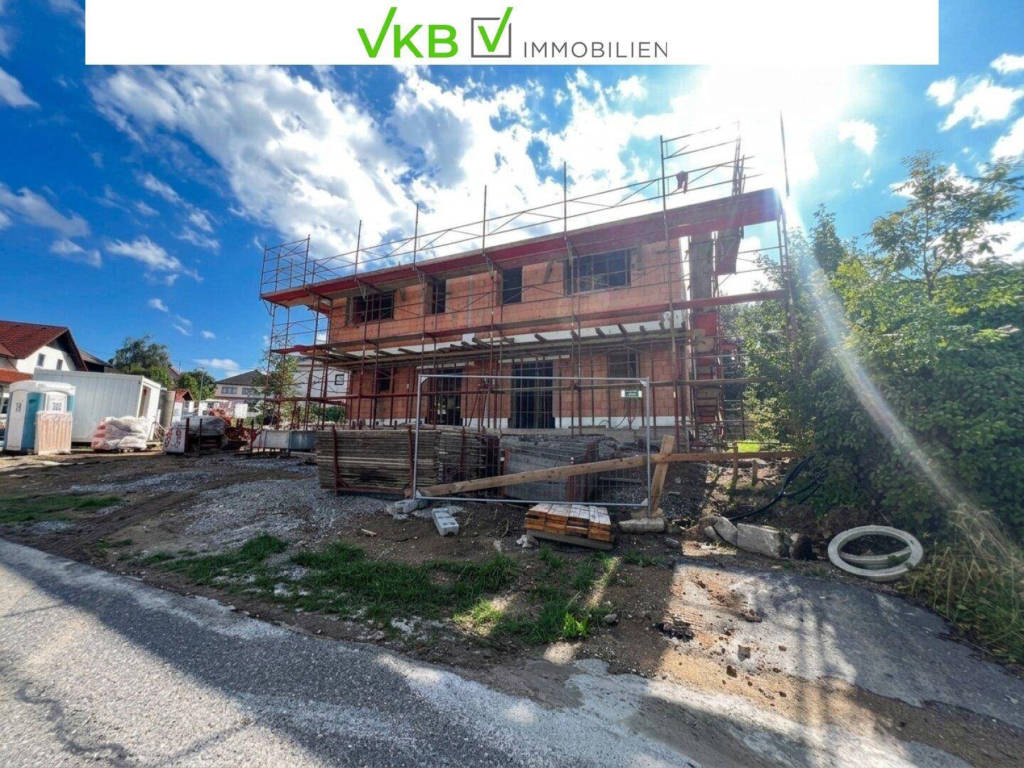 Neubau im Rohbauzustand mit Gerüst unter blauem Himmel und Sonnenschein auf der Baustelle.