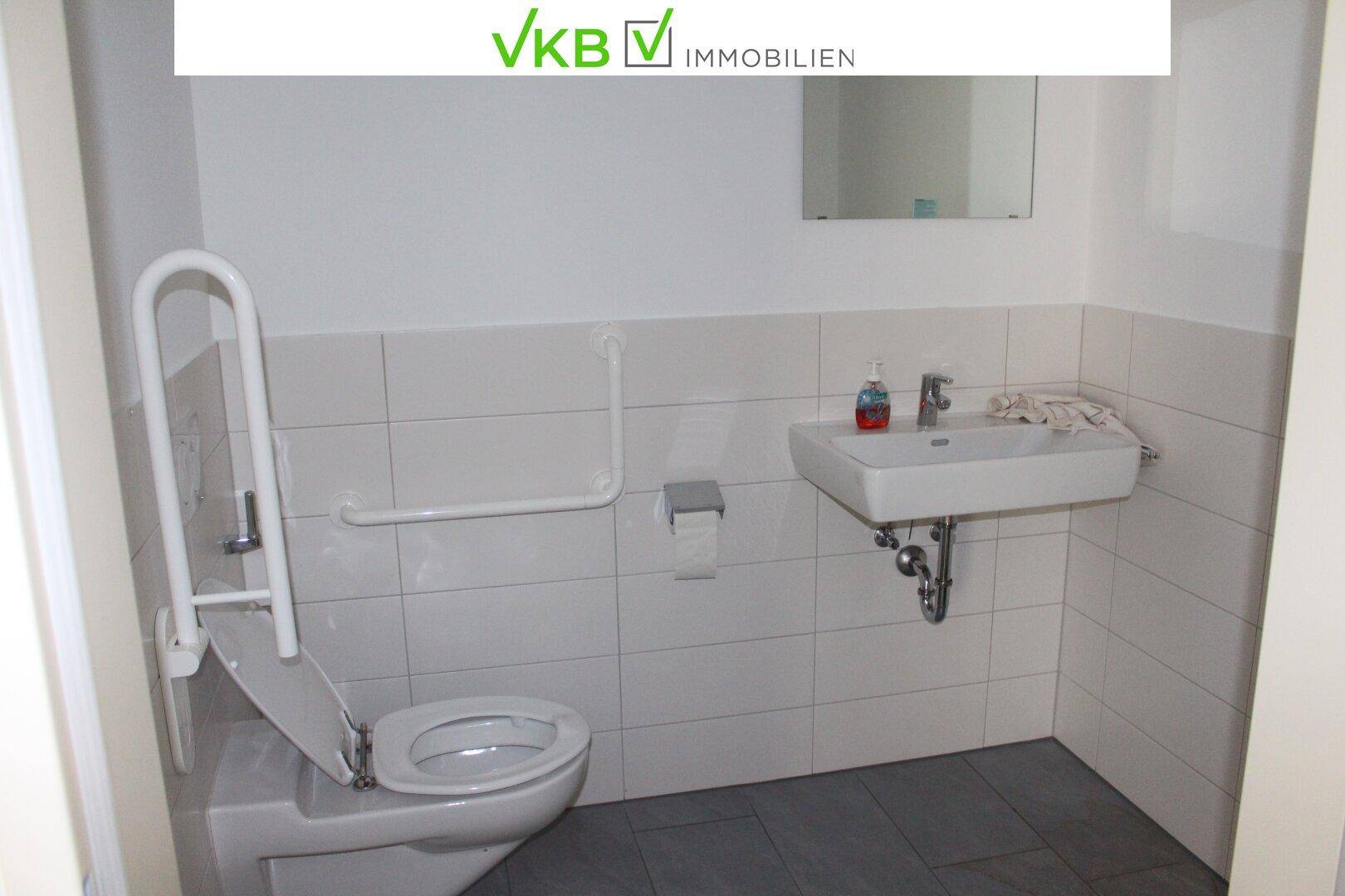 Barrierefreies Badezimmer mit WC, Waschbecken und Haltegriffen an den Wänden für mehr Sicherheit.