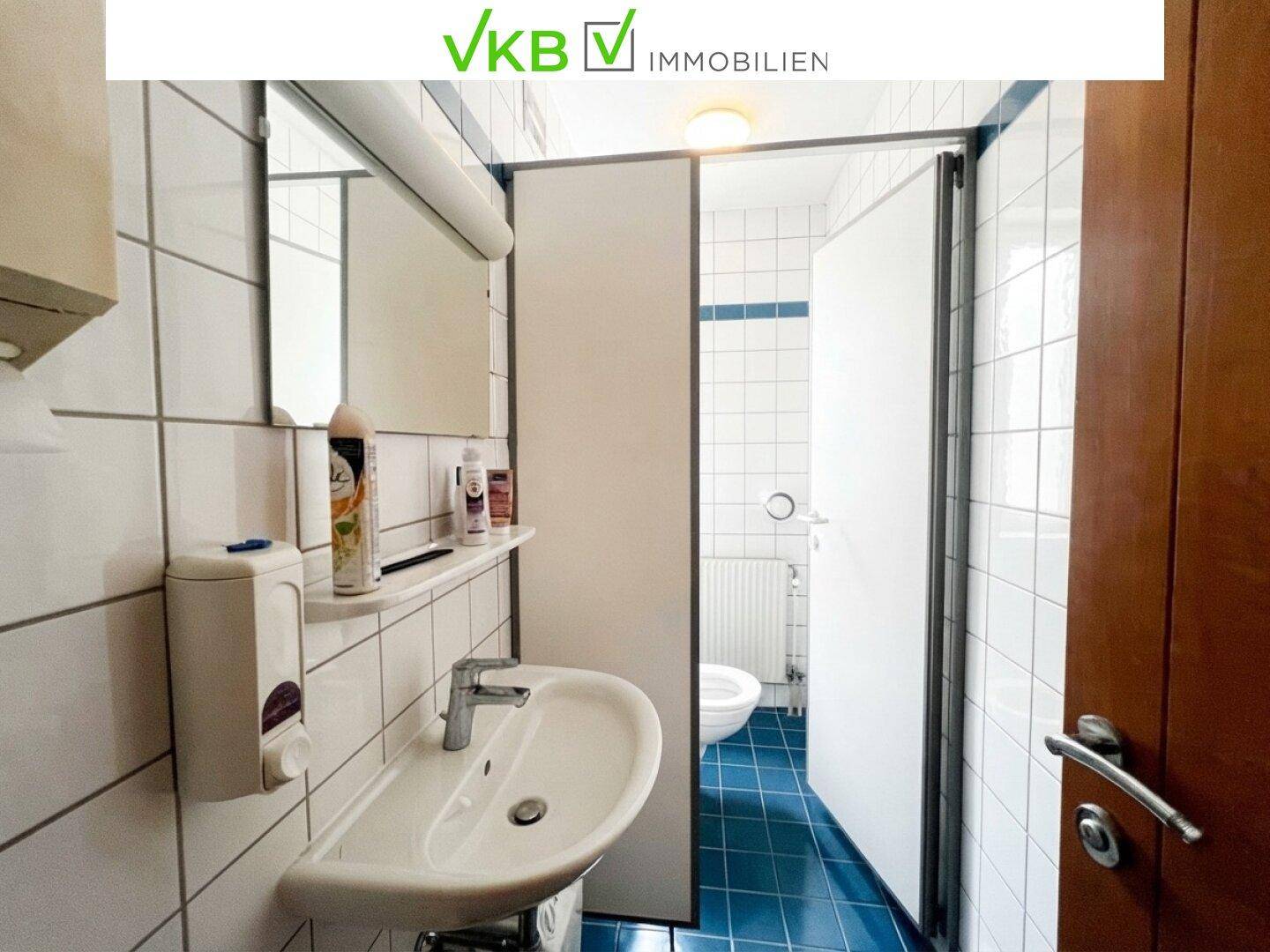 Kleines Badezimmer mit weißen Fliesen, blauem Boden und Waschbecken mit Spiegel.