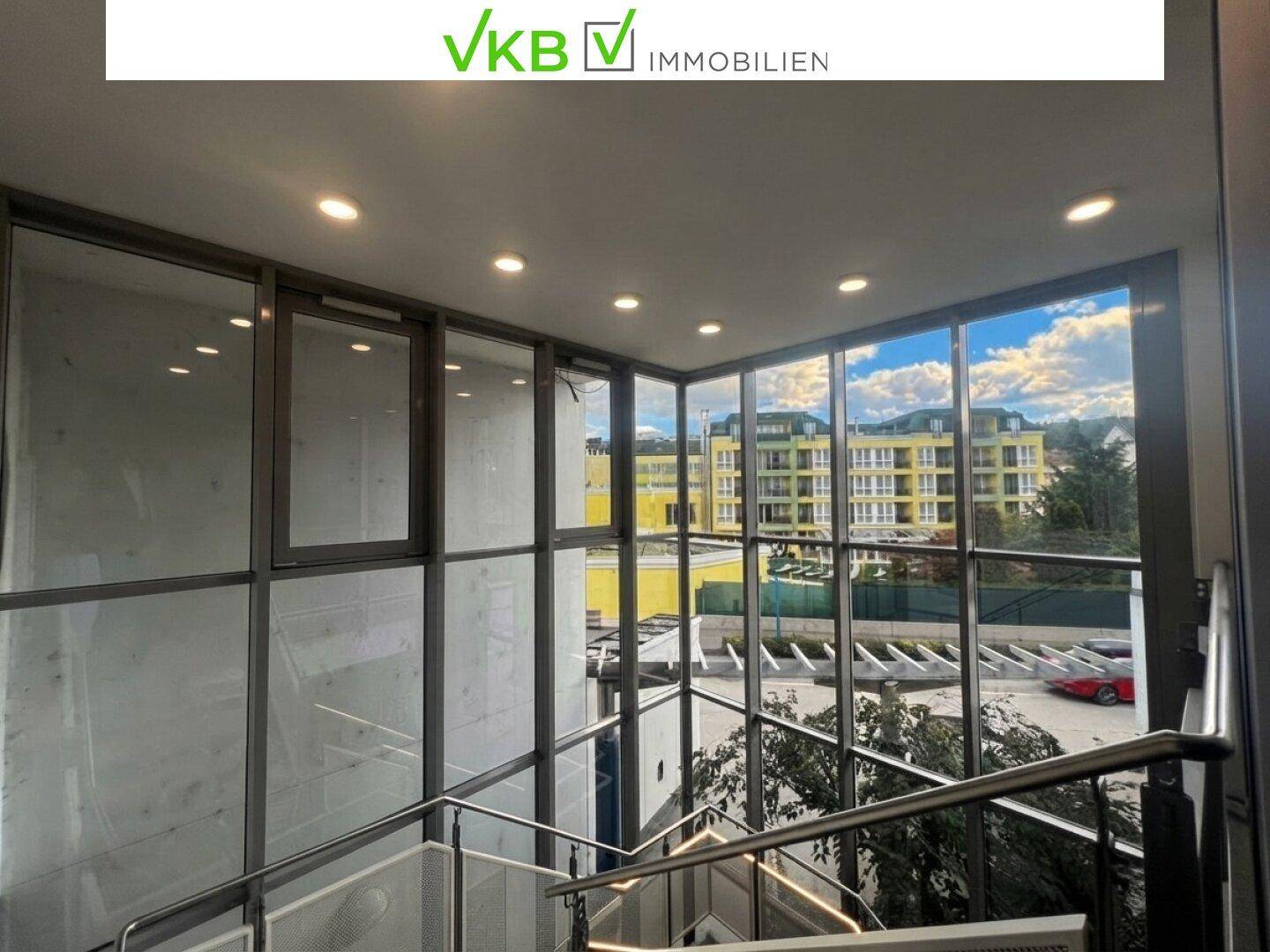 Moderner Treppenaufgang mit großen Glasfenstern und Blick auf umliegende Gebäude.