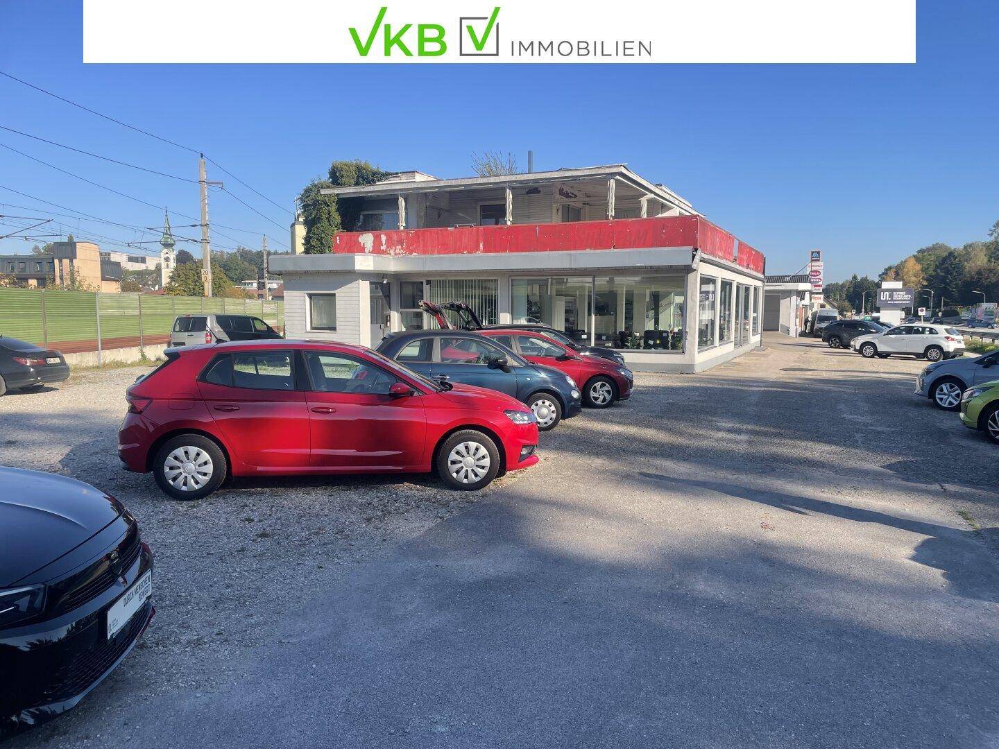 Außenansicht des Gebäudes mit einem großen Parkplatz voller Gebrauchtwagen unter blauem Himmel.