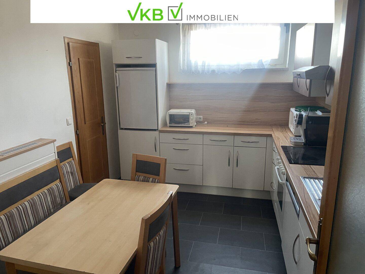 Kleine Küche mit Esstisch, weißen Schränken und Holztheke, ausgestattet mit Kühlschrank und Herd.