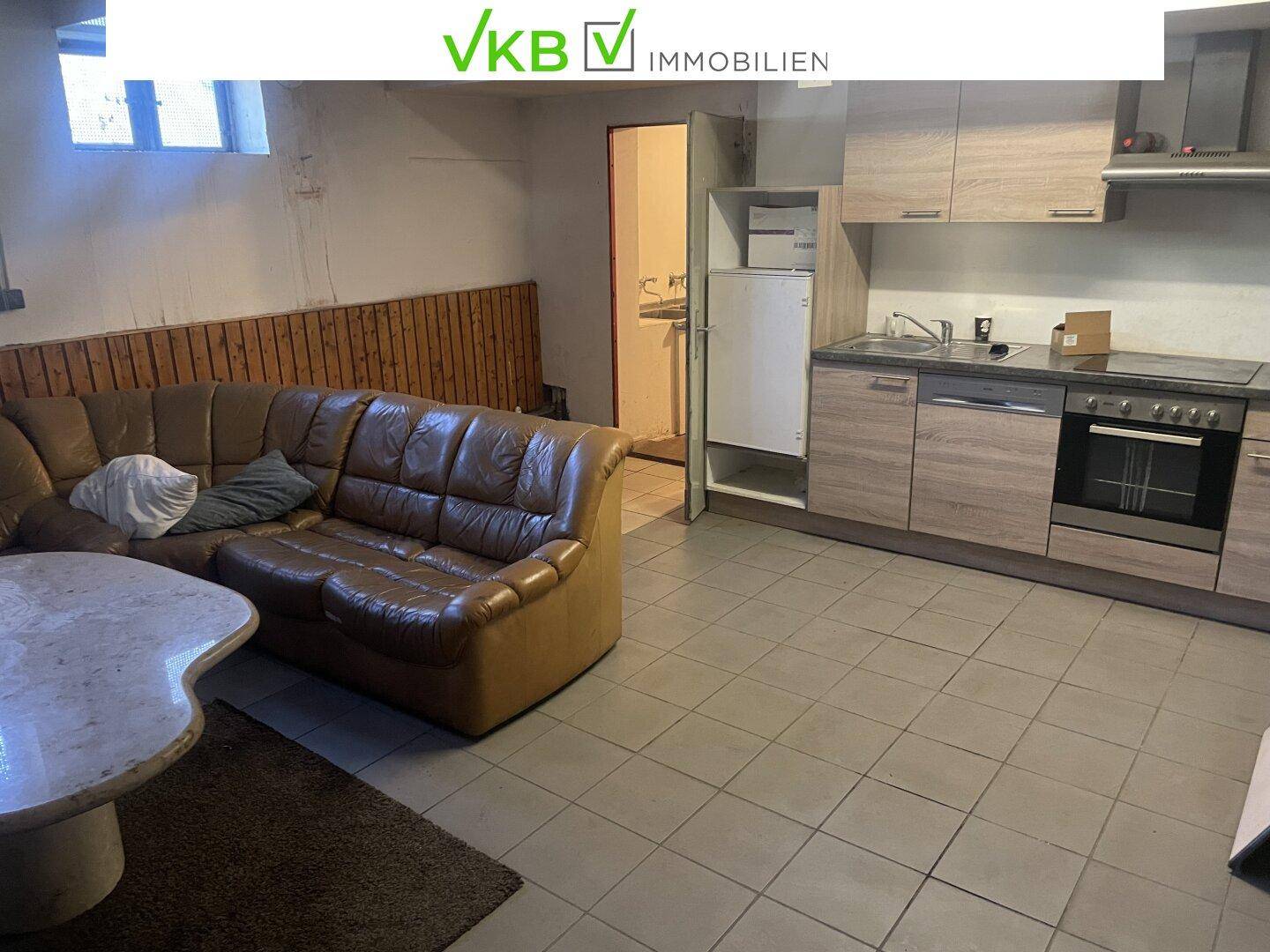Kombinierter Wohn- und Küchenbereich im Untergeschoss mit Sofa und einfacher Küchenzeile.