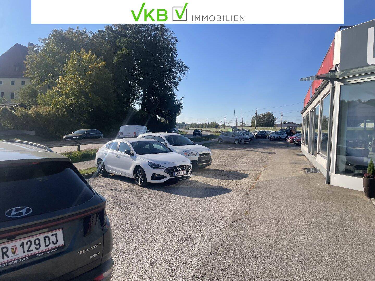 Außenbereich mit geparkten Fahrzeugen und einem Blick auf die umliegende Landschaft und Bäume.