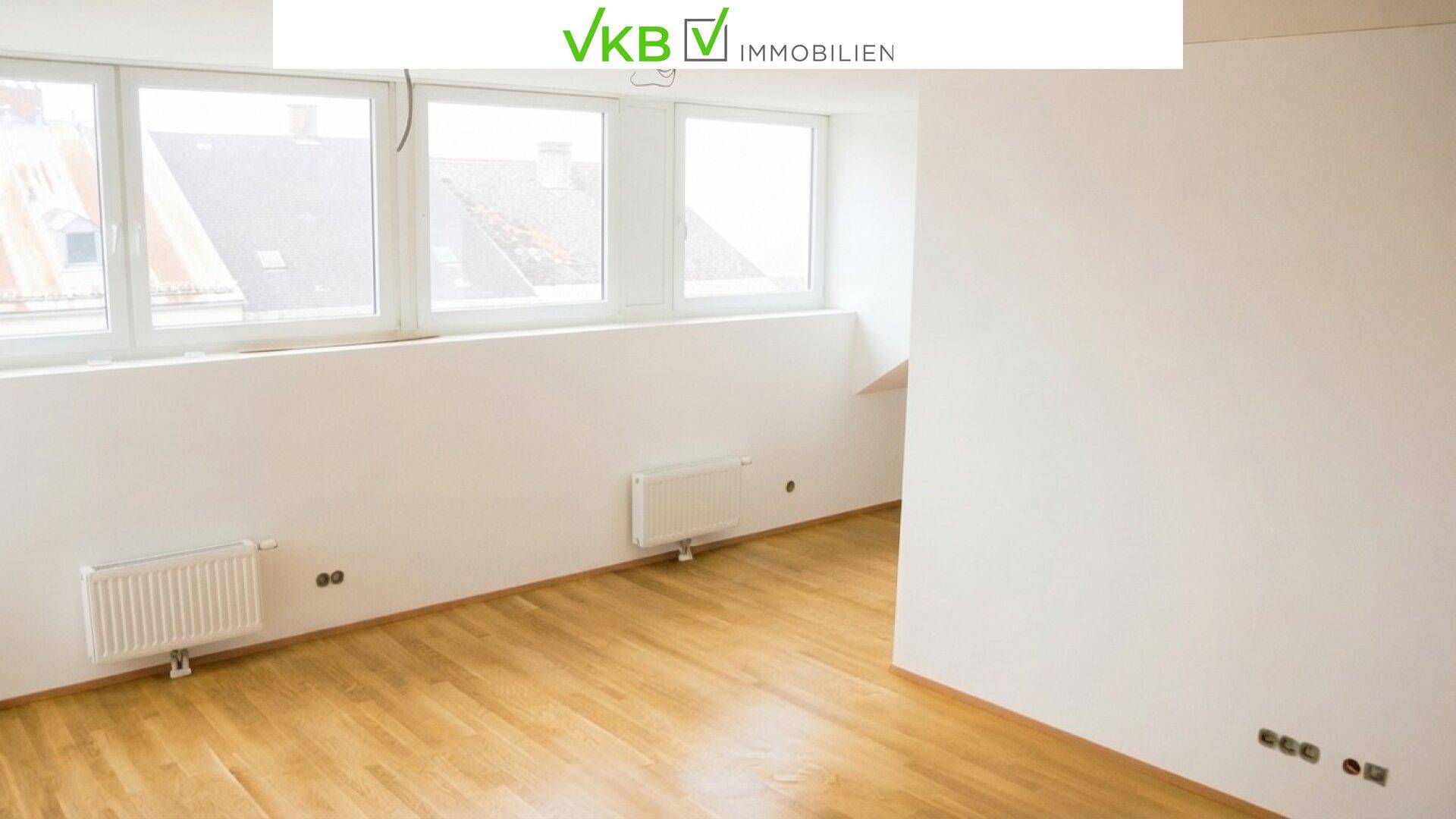 Leerer Raum mit Holzboden, Heizkörpern unter großen Fenstern und viel Tageslicht.