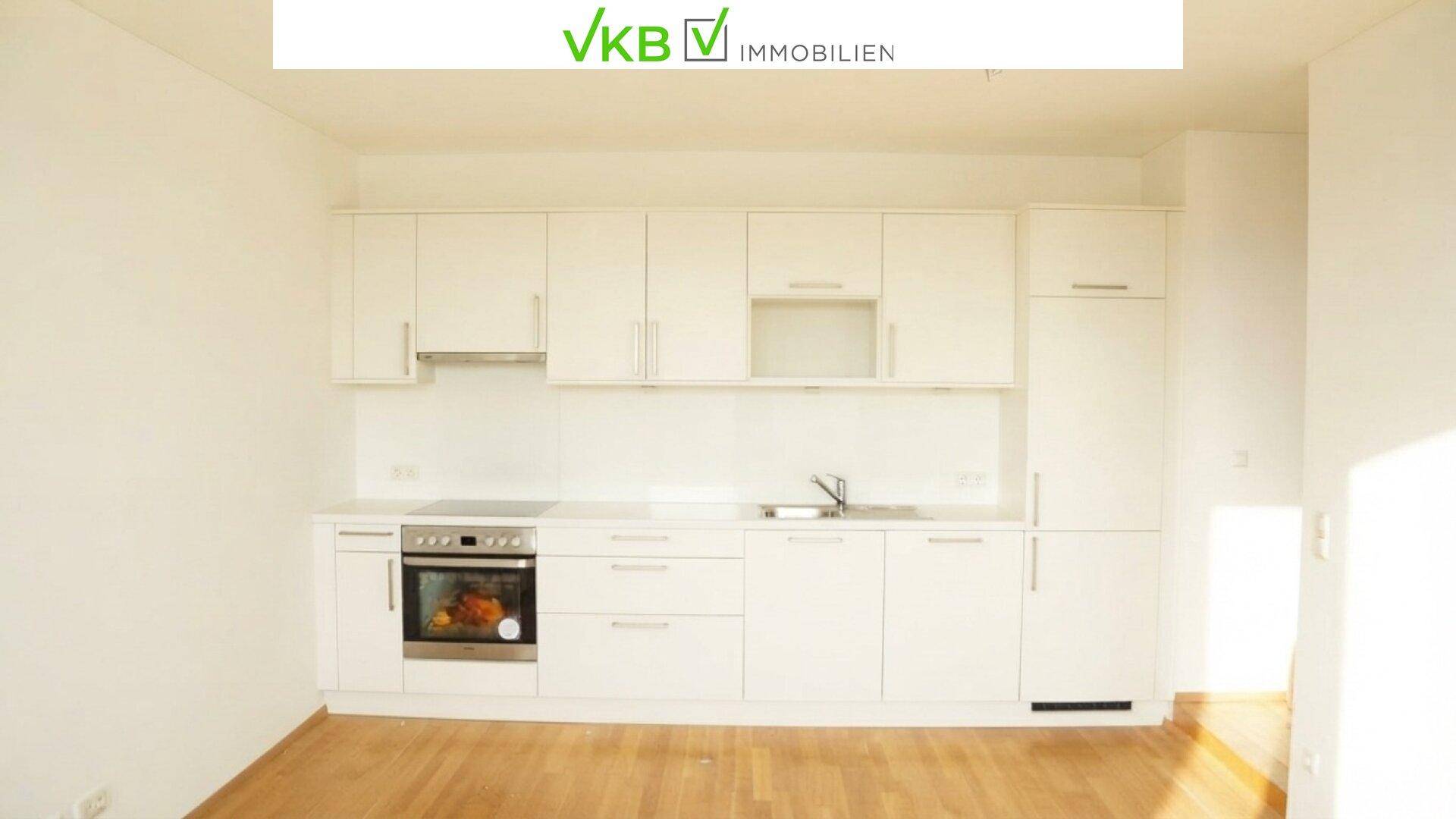 Helle, unmöblierte Küche mit weißen Schränken, integriertem Ofen und Holzboden.