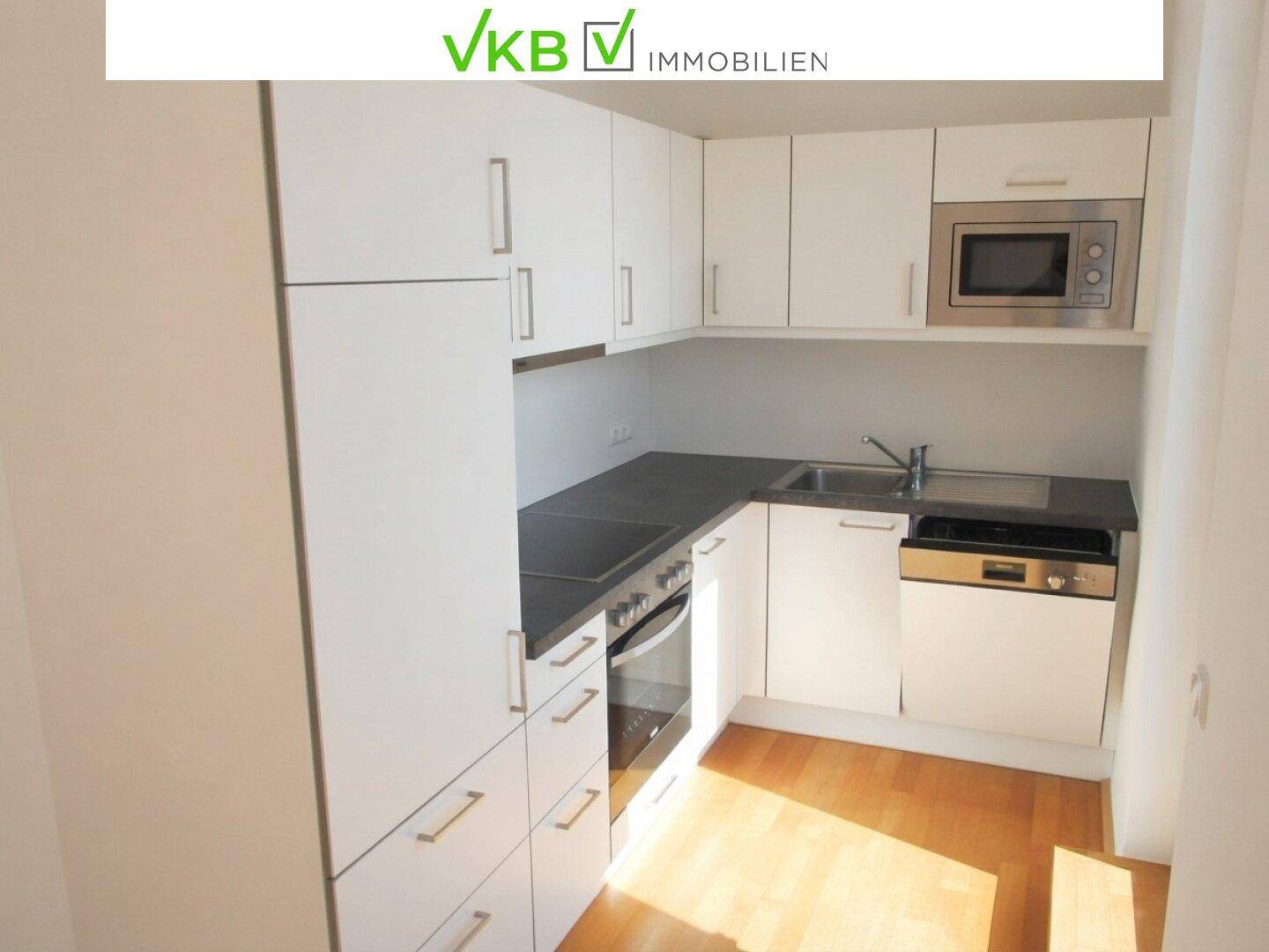 Moderne Einbauküche mit weißen Schränken, dunkler Arbeitsplatte und integrierten Elektrogeräten.