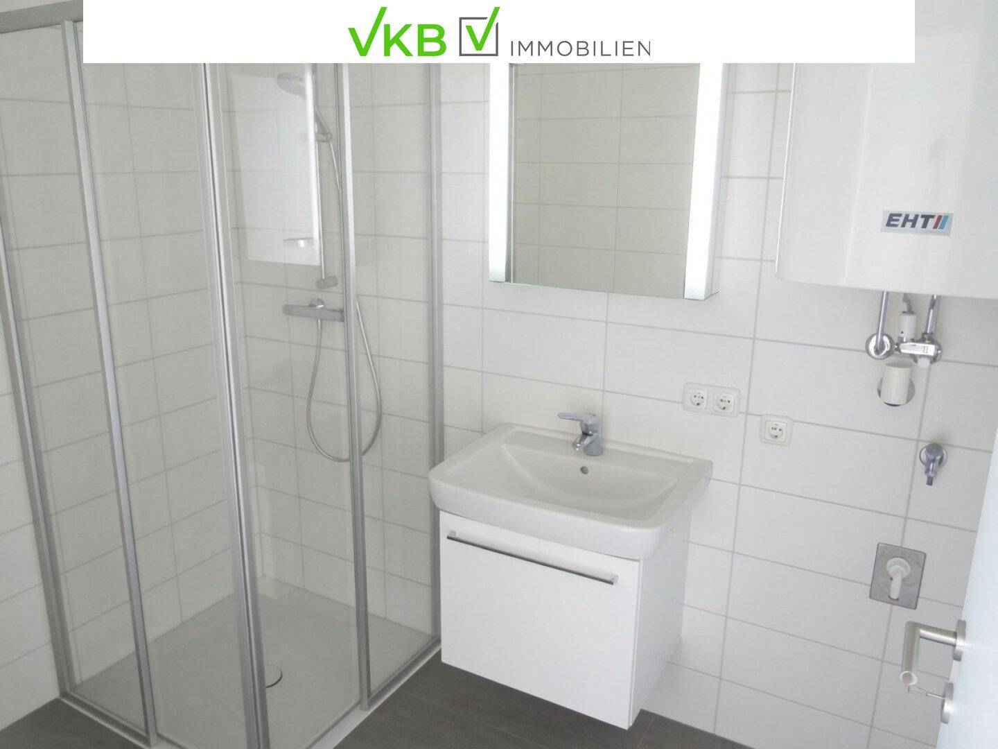 Modernes Badezimmer mit weißen Fliesen, einer Duschkabine und einem Waschtisch mit Spiegelschrank.
