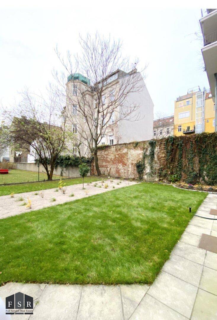 Gepflegter Gemeinschaftsgarten mit Rasenfläche und Bäumen, umgeben von einer alten Mauer.