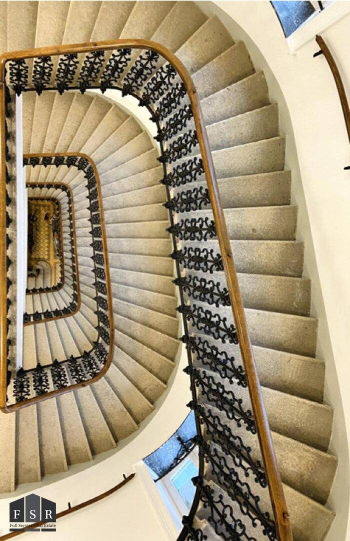 Blick von oben auf ein elegantes, spiralförmiges Treppenhaus mit Steinstufen und schmiedeeisernem Geländer.