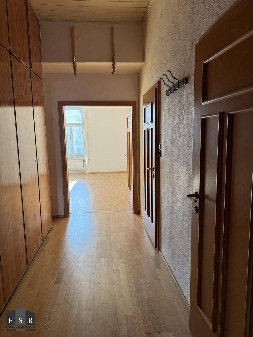 Heller Flur mit integrierten Holzschränken und Zugang zu einem weiteren Zimmer.