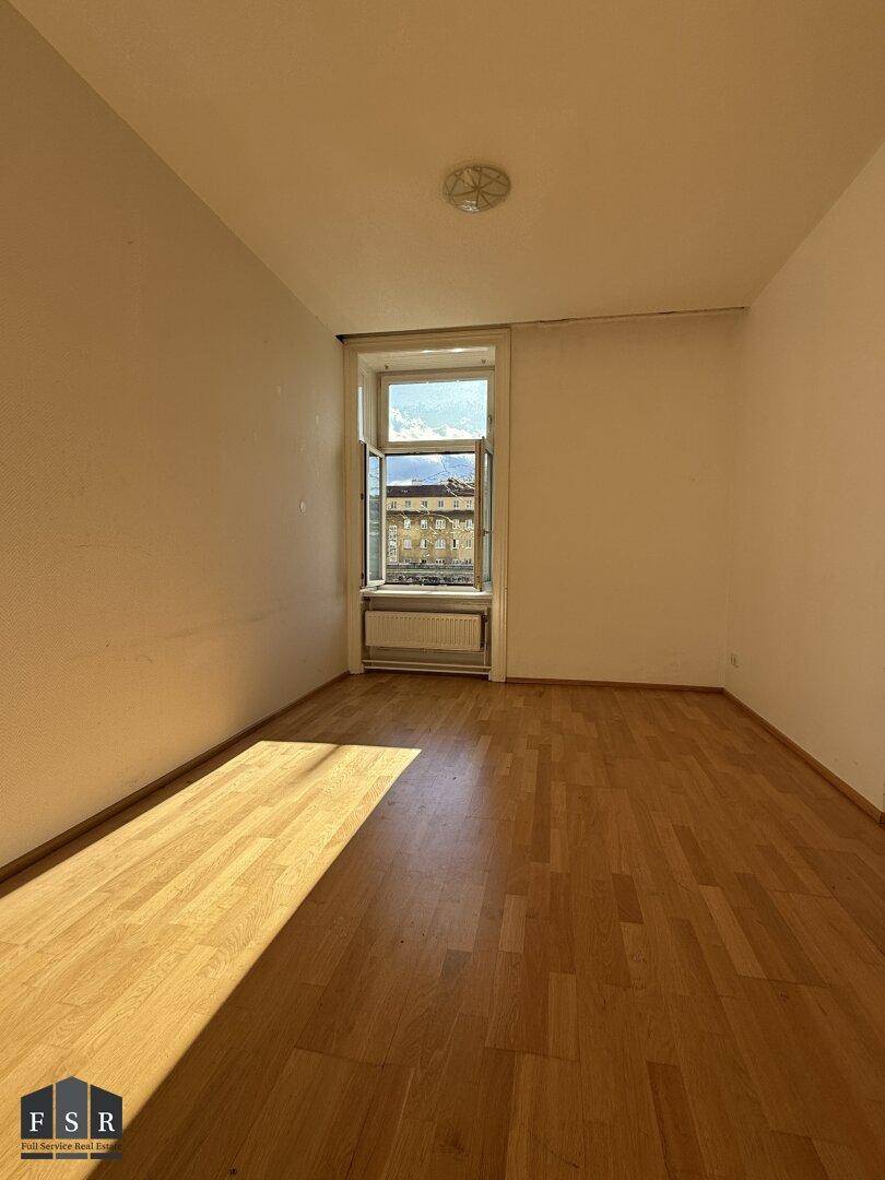 Helles Zimmer mit Parkettboden und weiß gestrichenen Wänden, mit Blick nach draußen.