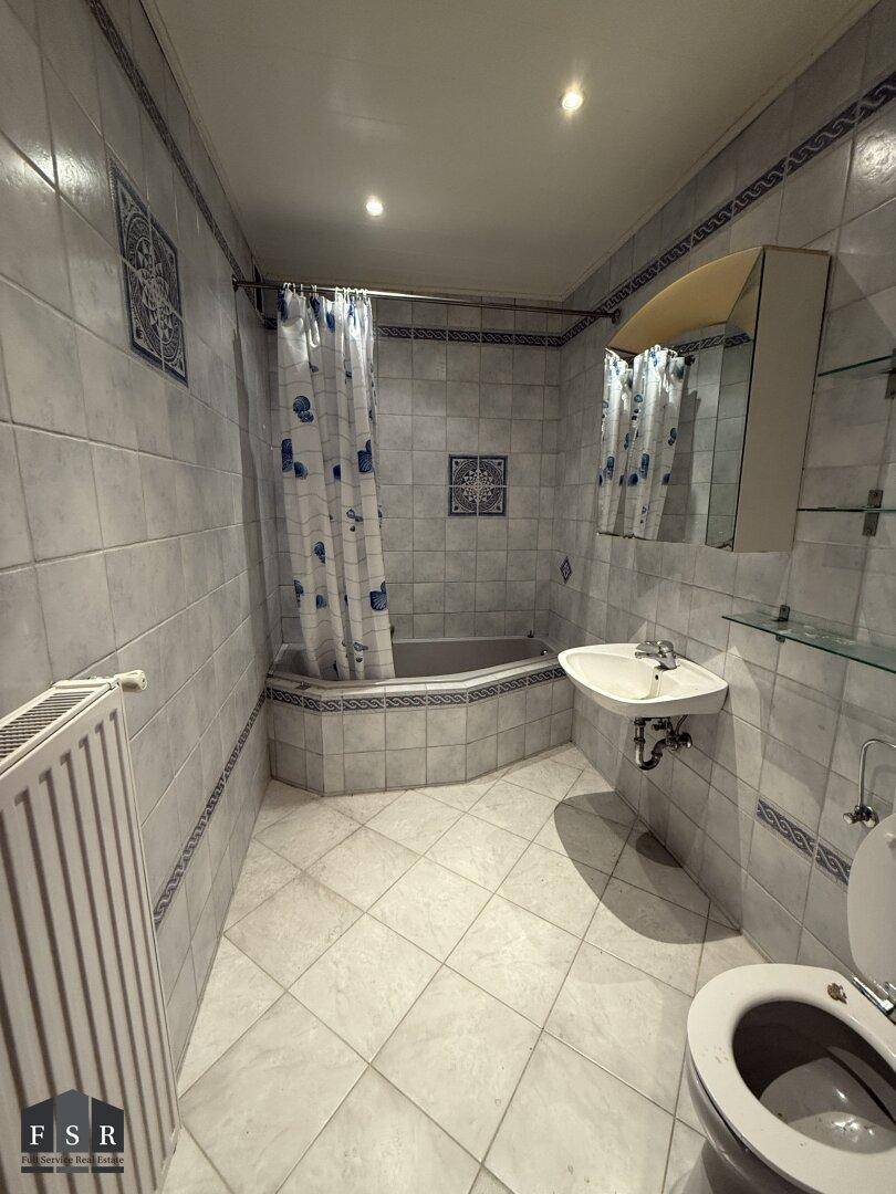 Badezimmer mit blauen und weißen Fliesen, Badewanne mit Duschvorhang und Waschbecken.