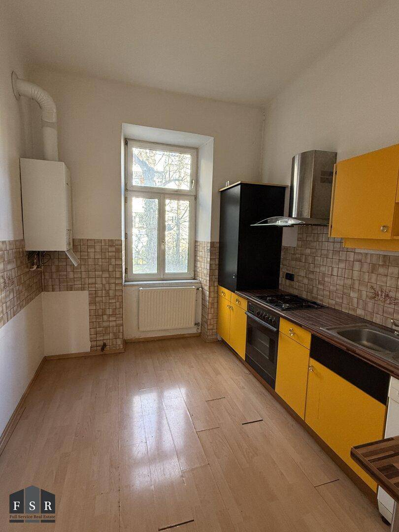 Küche mit gelben und schwarzen Schränken, Herd und Spüle, mit Fenster.