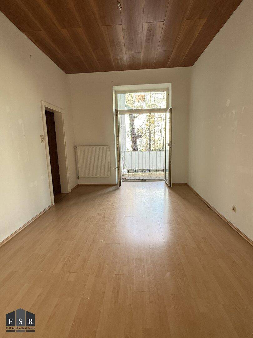 Heller Raum mit Holzboden und Holzdecke, mit Zugang zu einem französischen Balkon.