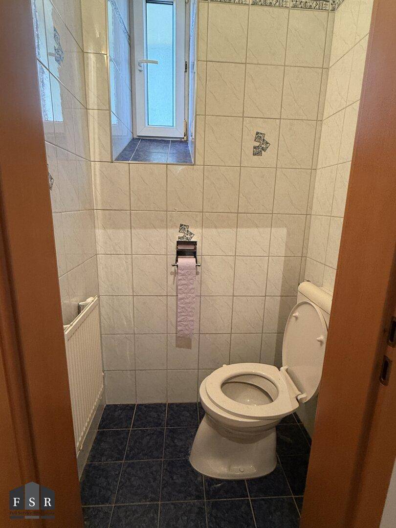 Kleines WC mit Toilette, Waschbecken und Fliesen an Wänden und Boden.