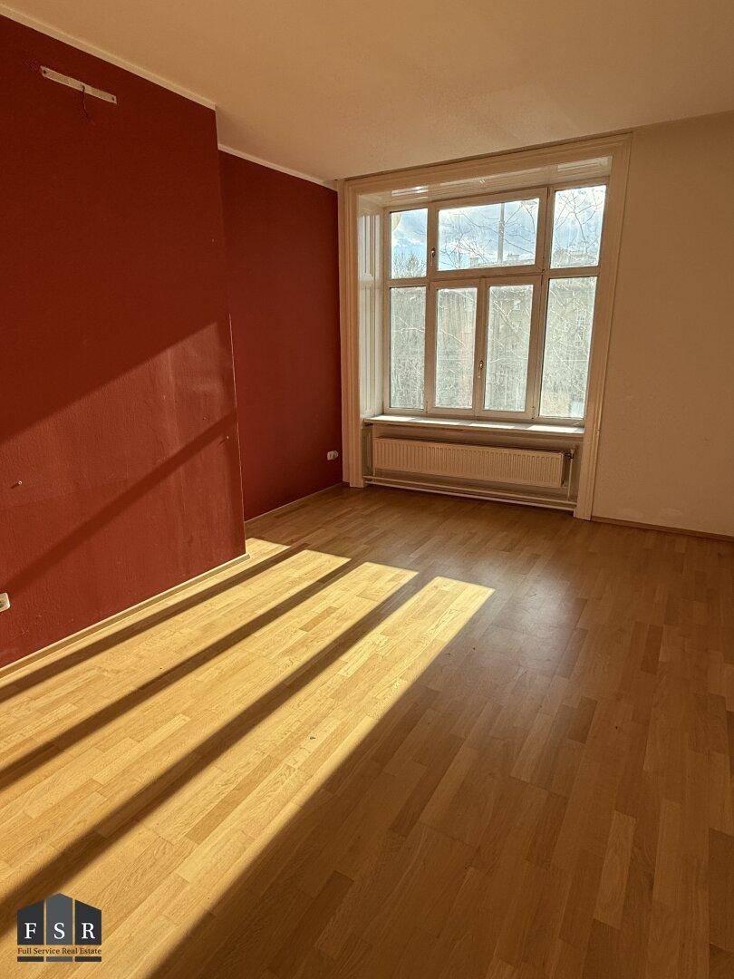Sonnenverwöhnter Wohnraum mit Parkettboden und einer roten Akzentwand, sehr hell.