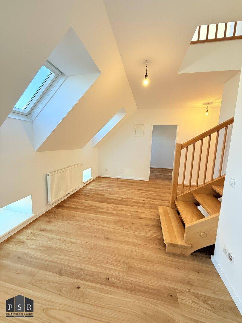 Geräumiger Wohnbereich im Dachgeschoss mit Holzboden, Dachfenstern und Zugang zur Treppe.