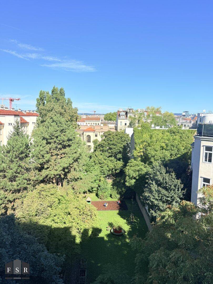Grüne Gartenanlage mit Bäumen und Rasenfläche, umgeben von Gebäuden in der Stadt.
