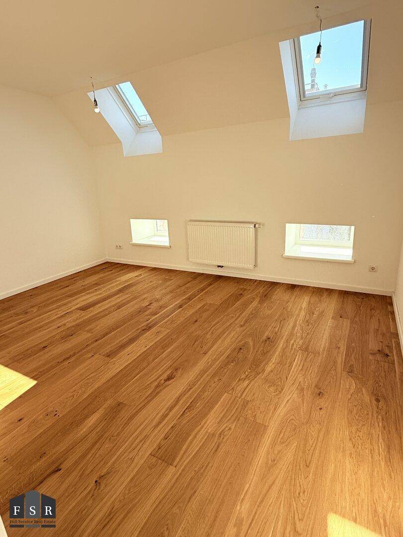 Helles Schlafzimmer im Dachgeschoss mit Holzboden, zwei Dachfenstern und viel Tageslicht.