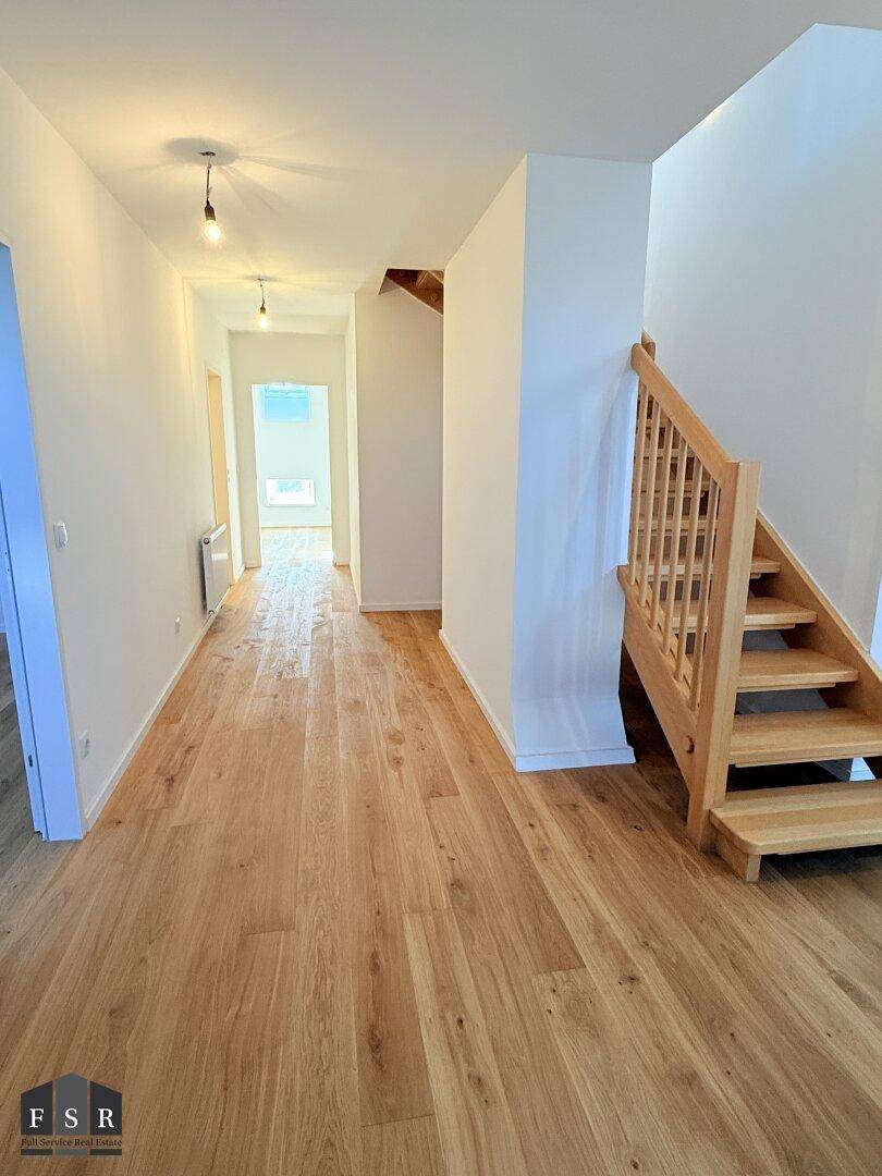 Heller Flur mit Holztreppe und durchgehendem Holzboden, der zu den oberen Etagen führt.