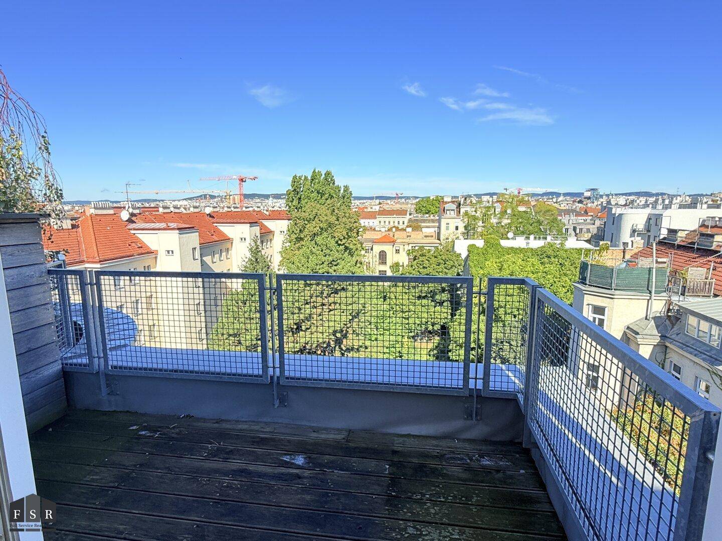 Geräumiger Balkon mit Holzboden und weitem Blick über die Stadt und grüne Umgebung.