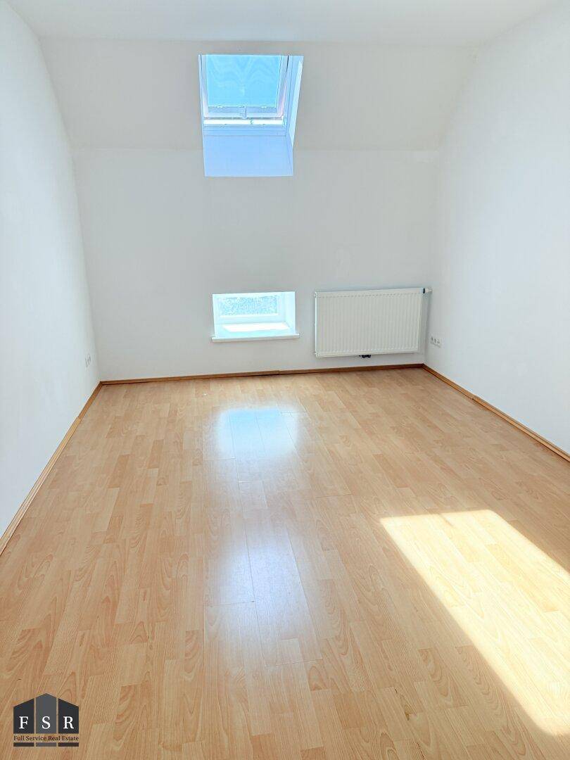 Freundliches Zimmer mit Laminatboden, Dachschräge und einem großen Dachfenster für viel Tageslicht.