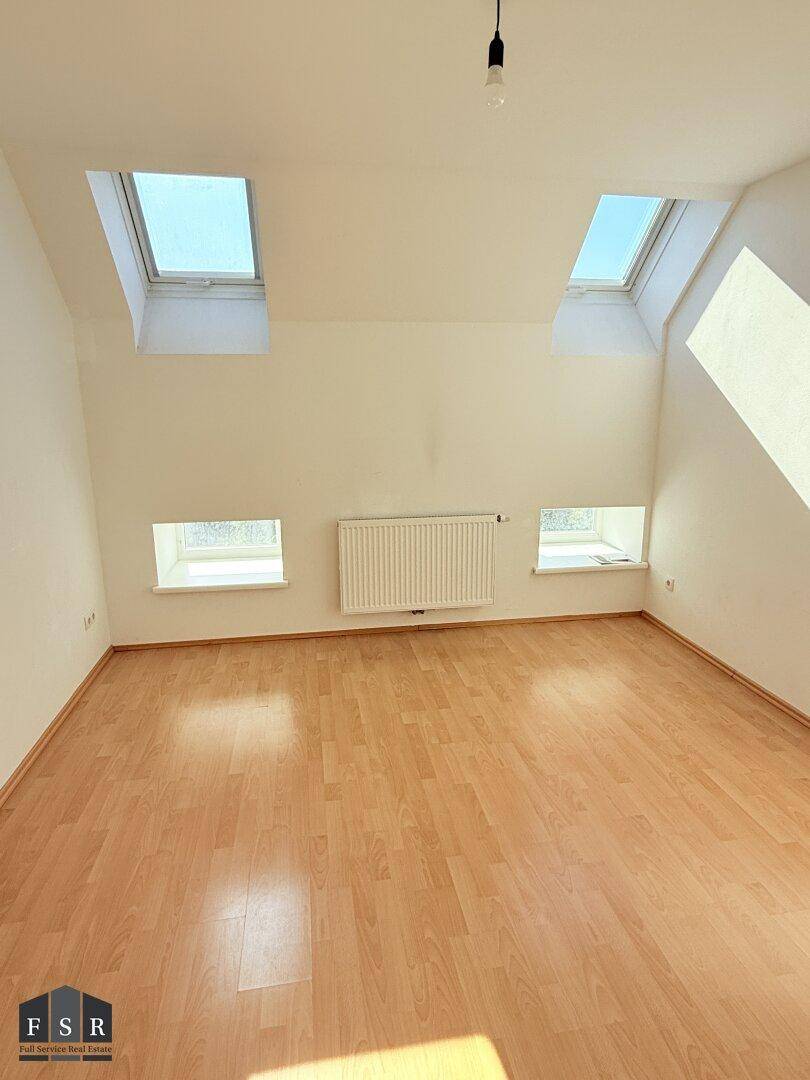 Helles Zimmer im Dachgeschoss mit Laminatboden, Dachschrägen und mehreren Dachfenstern.