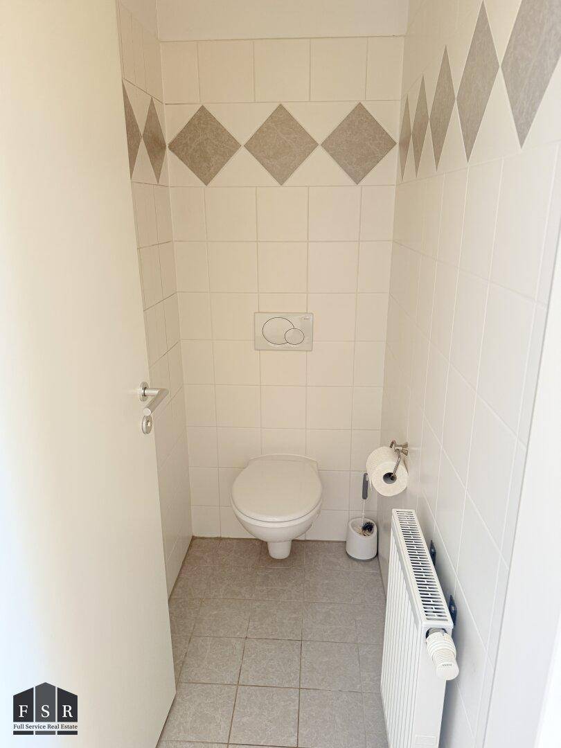 Separates WC mit Wand-WC, Heizkörper und Fliesen in Weiß und Beige.