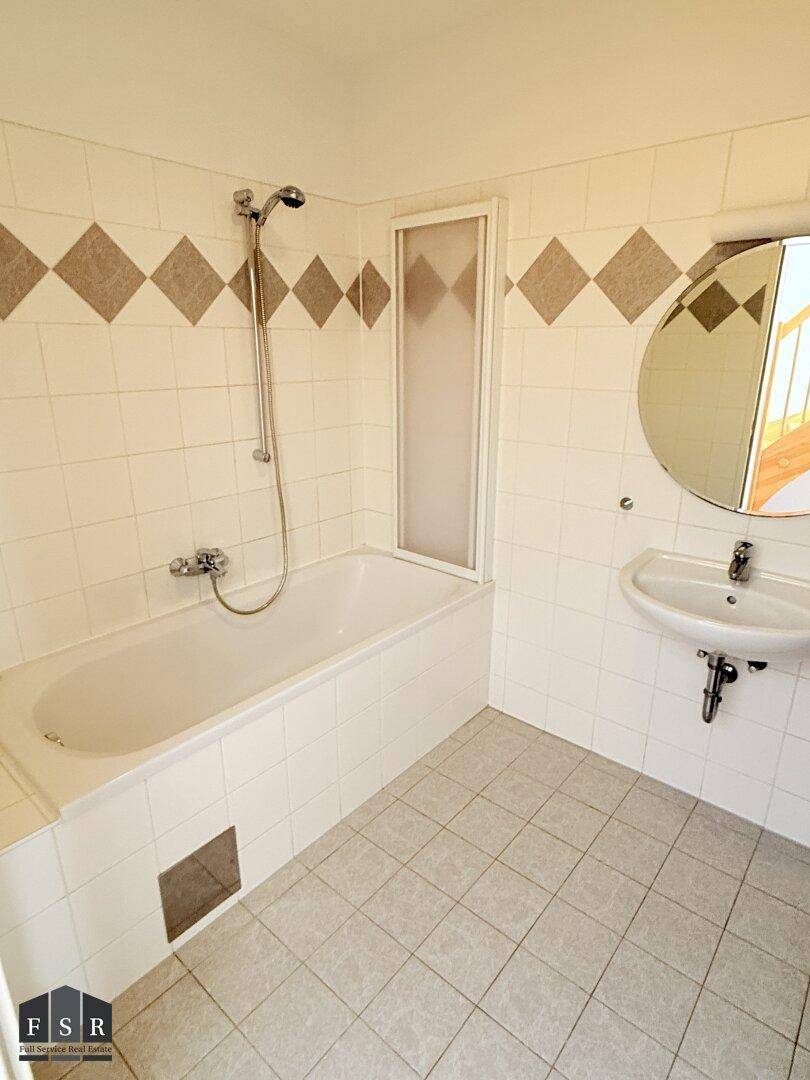 Badezimmer mit Badewanne, Waschbecken und Fliesen in Weiß und Beige mit dekorativen Akzenten.