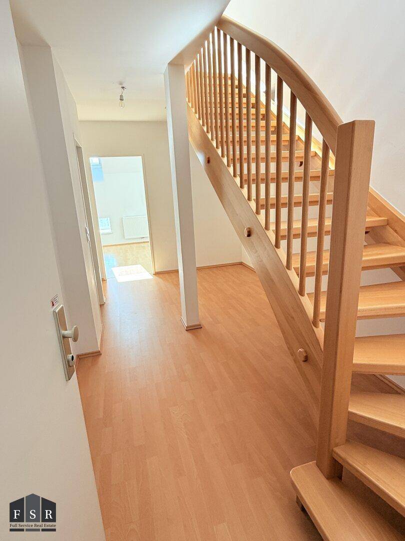 Heller Flur mit Holztreppe und Laminatboden, der zu weiteren Räumen führt.