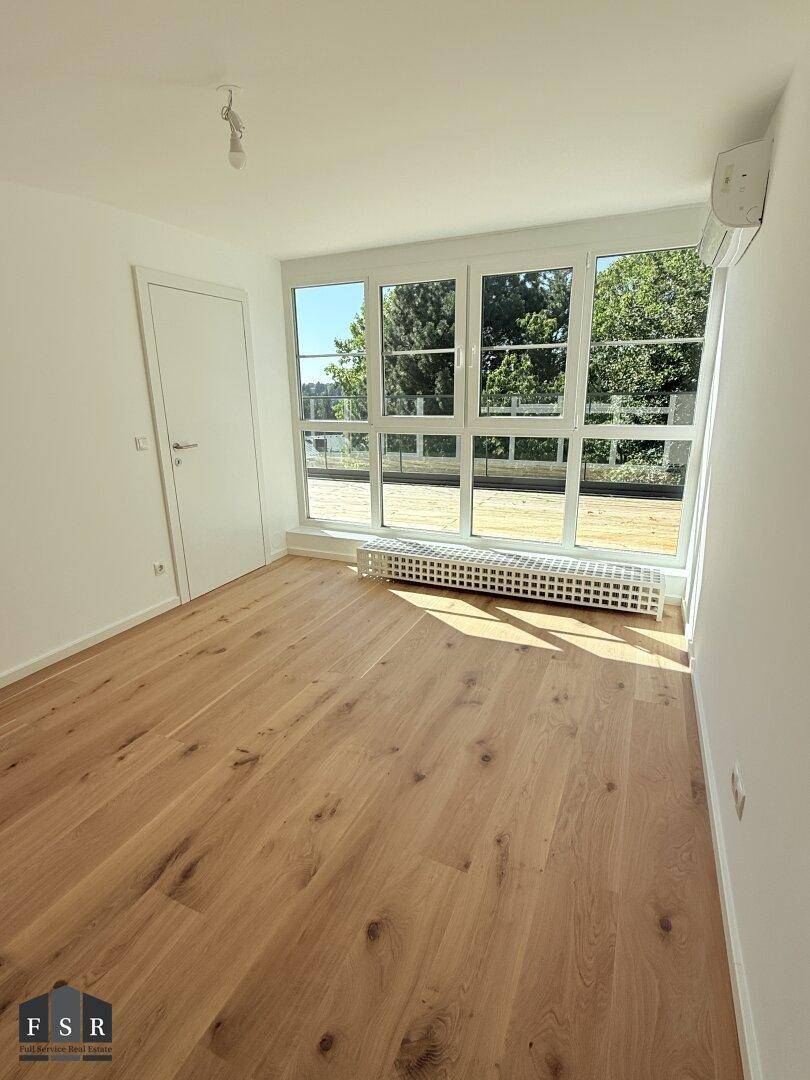 Helles Schlafzimmer mit Holzboden, großen Fenstern und Klimaanlage.