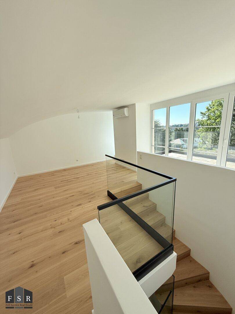 Heller Dachgeschossraum mit Holzboden, Schrägen und moderner Treppe mit Glasgeländer.