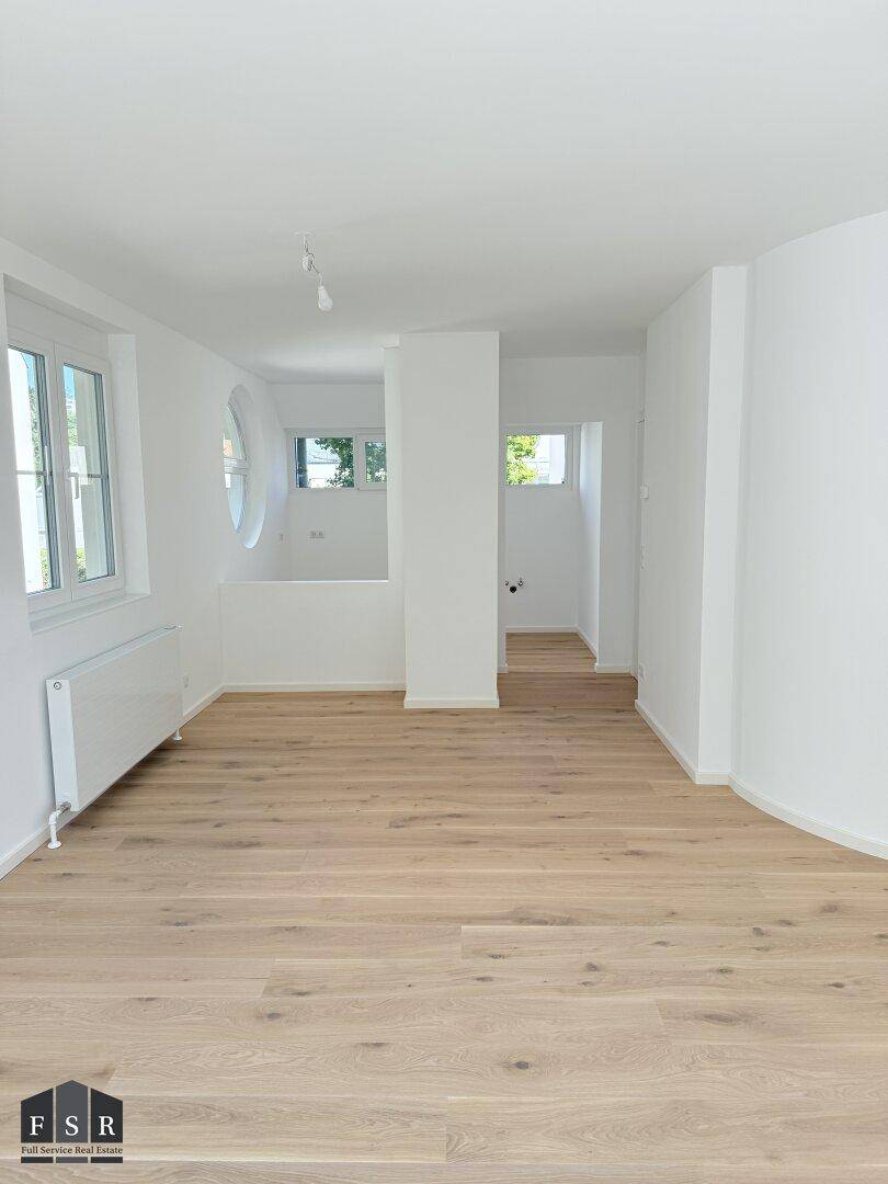 Geräumiger Wohnbereich mit Holzboden, runden Fenstern und offener Raumgestaltung.