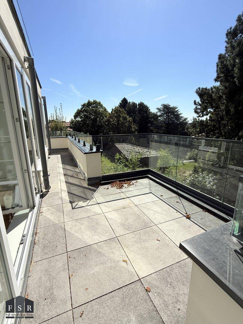Große geflieste Terrasse mit Glasgeländer und Blick auf die Umgebung.