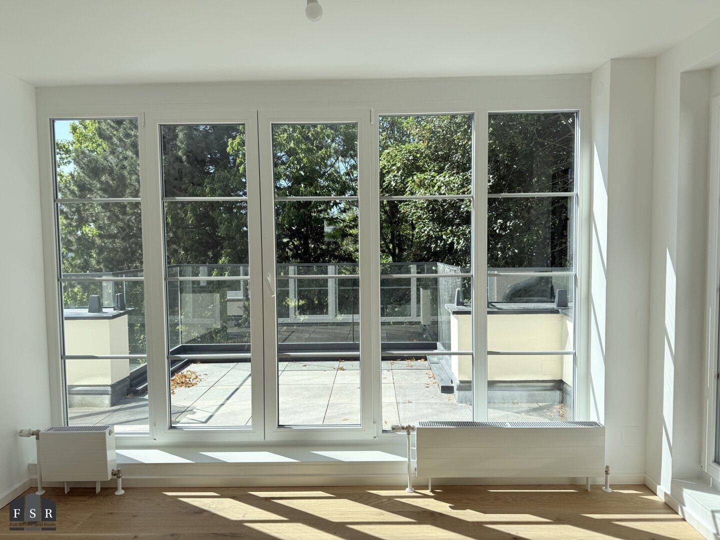 Lichtdurchfluteter Wohnbereich mit Holzboden und großen Fenstern zur Terrasse.