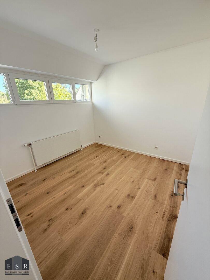 Helles Schlafzimmer mit Holzboden und mehreren Fenstern für viel Tageslicht.