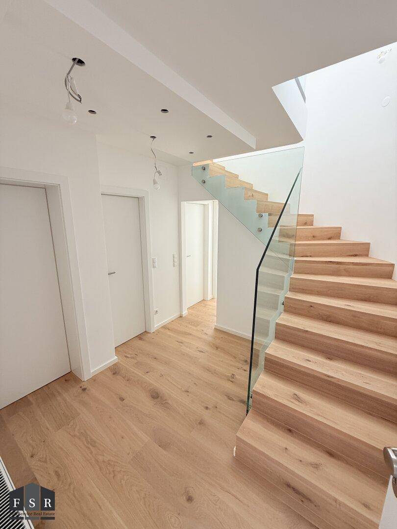 Moderner Flur mit Holztreppe, Glasgeländer und Einbaustrahlern.