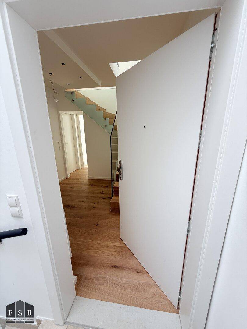 Heller Eingangsbereich mit moderner weißer Tür und Blick auf die Holztreppe.