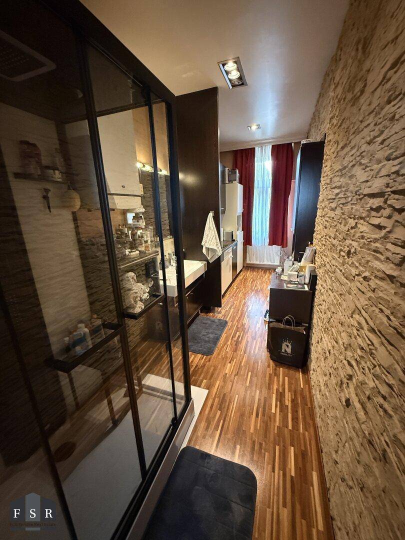 Langes Badezimmer mit Steinwand, Duschkabine und Holzparkettboden, gut beleuchtet.