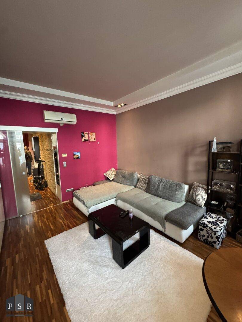 Gemütliches Wohnzimmer mit Ecksofa, Holzboden und einer auffälligen pinken Akzentwand.