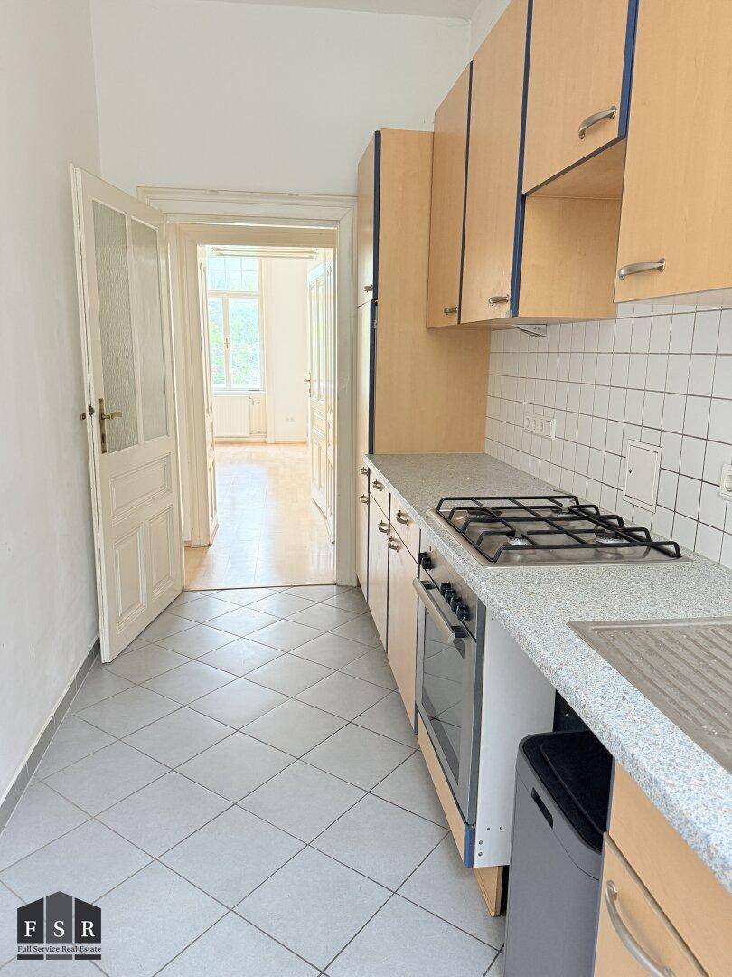 Funktionale Küche mit hellen Holzschränken, Gasherd und Blick in ein weiteres Zimmer.