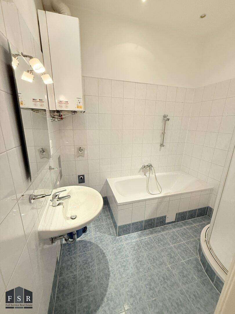 Badezimmer mit Badewanne, Waschbecken und weißen sowie blauen Fliesen.