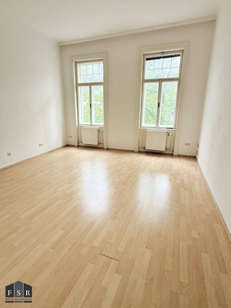 Helles Zimmer mit Laminatboden, zwei großen Fenstern und Blick ins Grüne.