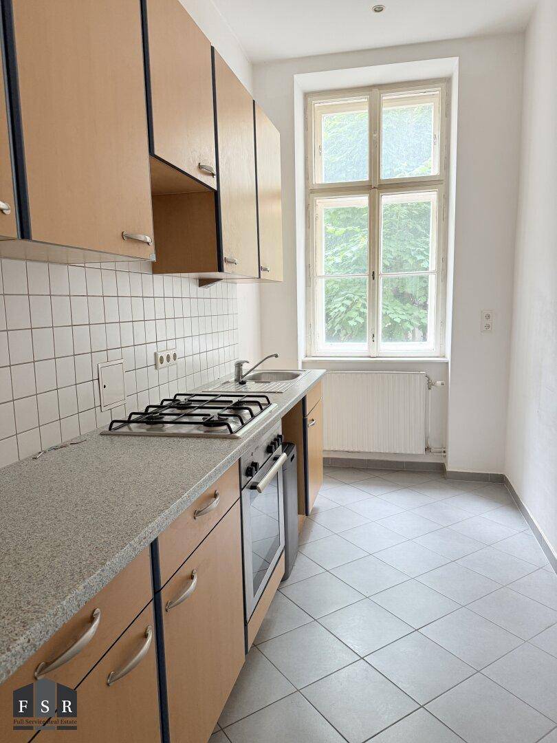 Funktionale Küche mit hellen Holzschränken, Gasherd und Fenster mit Blick ins Grüne.