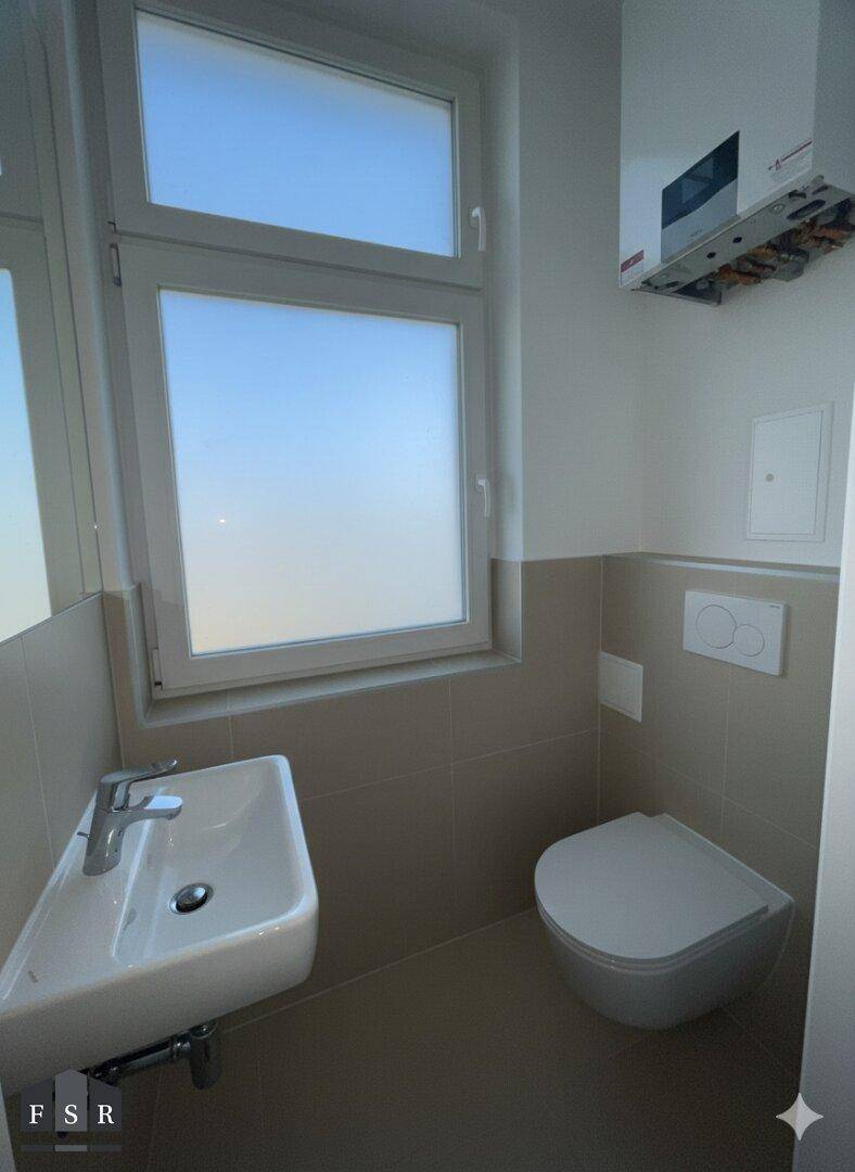 Modernes Gäste-WC mit Wand-WC, kleinem Waschbecken und Fenster für natürliche Belüftung.
