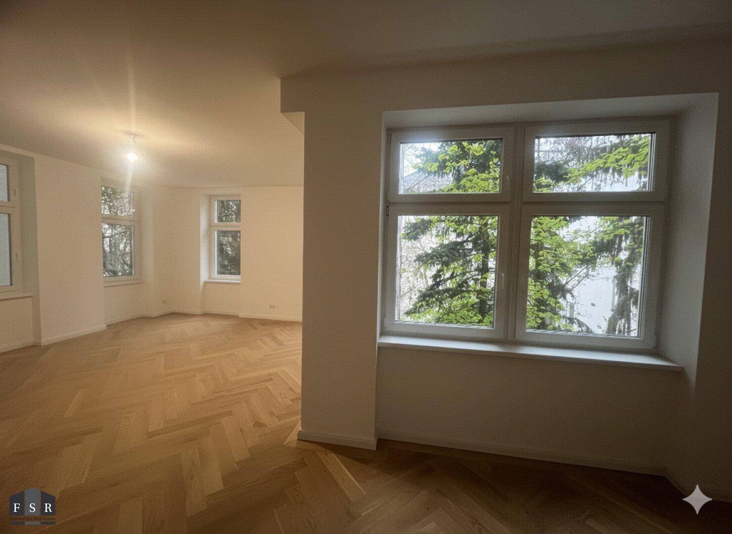 Großzügiger Wohnbereich mit Fischgrätparkett und Blick ins Grüne durch die großen Fenster.