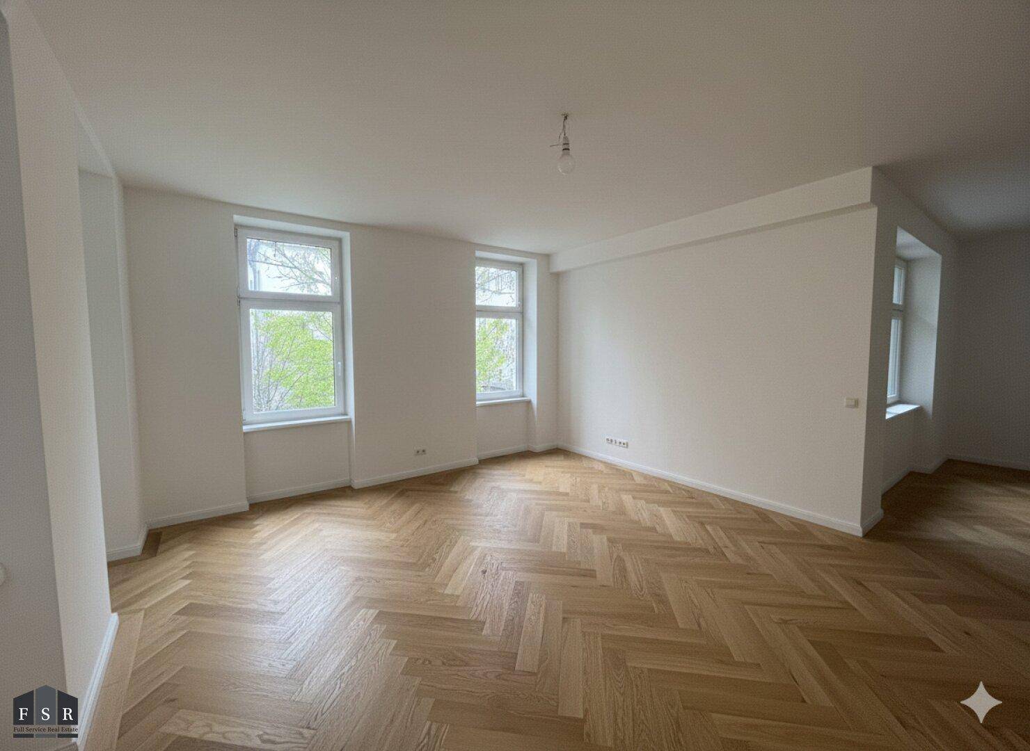 Heller und geräumiger Wohnbereich mit Fischgrätparkett und mehreren Fenstern, die den Raum erhellen.