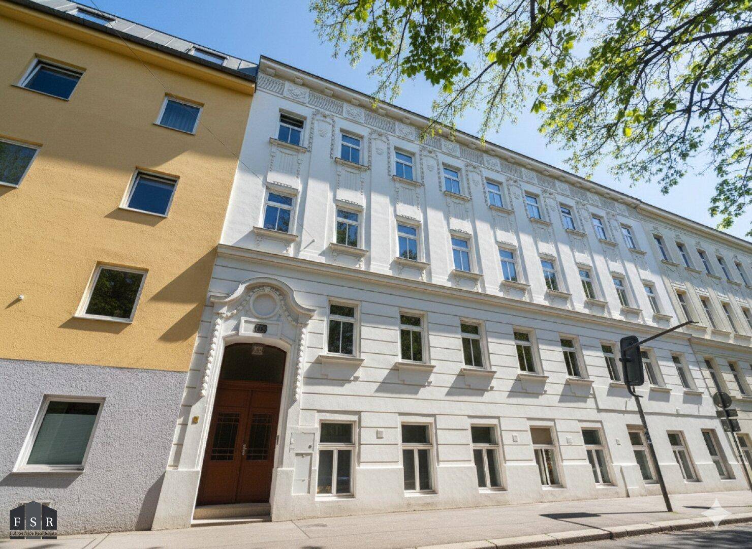 Historisches Gebäude mit klassischer Fassade und vielen Fenstern in einer städtischen Umgebung.