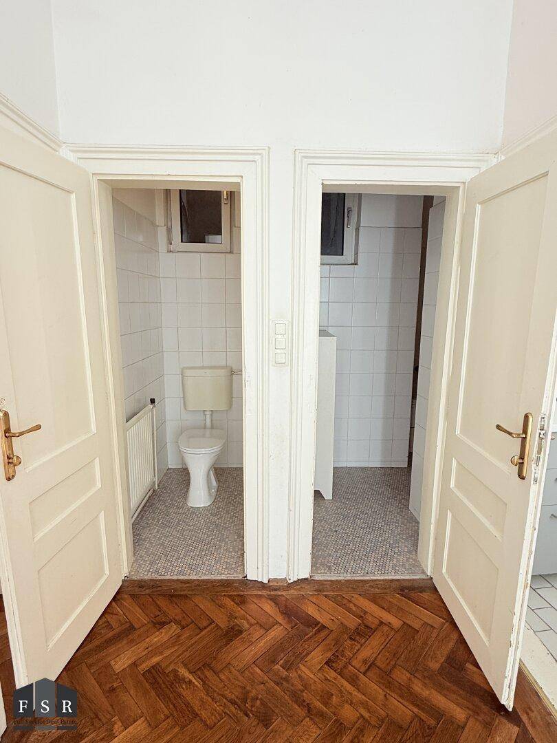 Zwei separate kleine Räume, einer davon als WC mit Fenster und Fliesenboden, in einem Altbau.